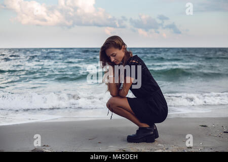 Junge Frau Hockend von Water's Edge am Strand, Odessa, Odessa, Ukraine Stockfoto