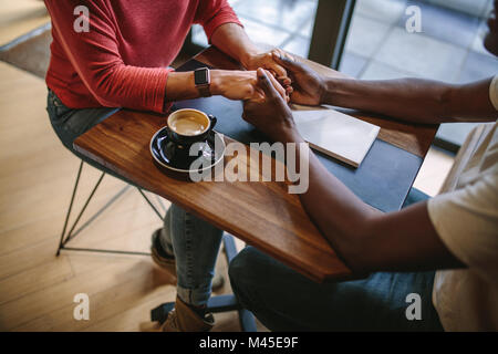 Der Mann und die Frau sitzt an einem Tisch, Hände halten mit einer Tasse Kaffee auf dem Tisch. Zugeschnittenes Bild des Menschen halten sich an den Händen einer Frau sitzt an einem Co Stockfoto