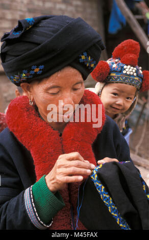 Laos. (In der Nähe von Luang Namtha Muang Sing). Yao Hill Tribe (Mien Stamm). Frau sticken eigene Kleidung. Neugierig Baby. Porträt. Stockfoto