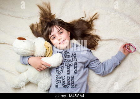Süße kleine Mädchen umarmte ihre Spielzeug liegend auf Bett Stockfoto