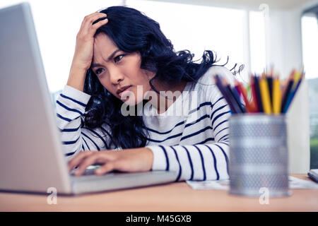 Konzentrierte Asiatin mit Hand am Kopf mit laptop Stockfoto