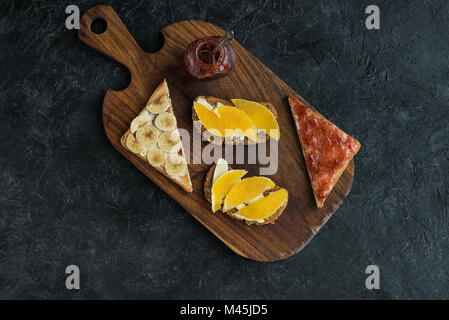 Flach mit Snacks für gesundes Frühstück auf Holz Schneidebrett auf dunklen Tischplatte Stockfoto