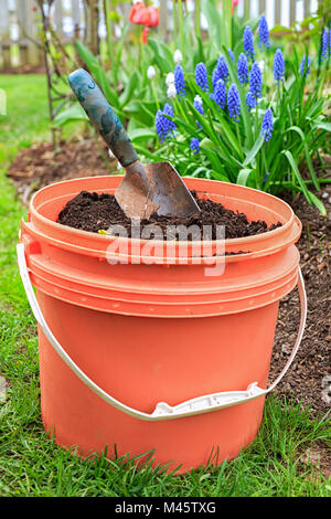 Ein Eimer voller Kompost mit einem Garten Kelle im heimischen Garten. Stockfoto