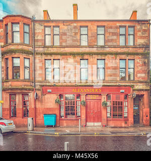 Ein roter Sandstein Mietshaus am unteren Ende von Alexander street in Clydebank mit der Street Bar im Erdgeschoss. Stockfoto