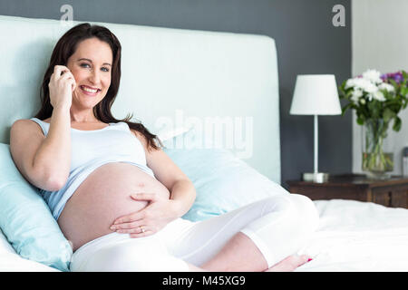 Schwangere Frau im Bett einen Anruf tätigen Stockfoto