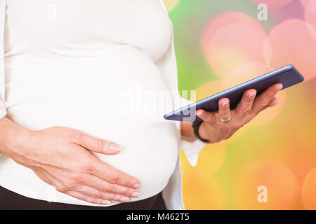 Zusammengesetztes Bild der Mittelteil der schwangeren Frau mit Tablet-PC Stockfoto