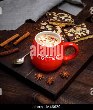 Schwarzen Kaffee mit Marshmallow in einem roten Keramik Tasse auf einem Braunen board und Schokolade Gebäck mit Mandeln Stockfoto