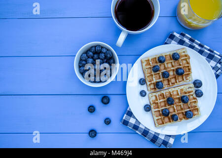 Waffeln und Blaubeeren Frühstück mit Kaffee und Orangensaft Overhead auf Blau Holz Tisch Hintergrund Stockfoto