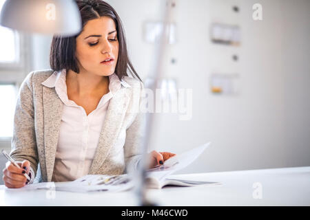 Geschäftsfrau lesen Broschüre während Notizen im Büro Stockfoto