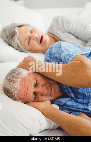 Senior Manndeckung ihre Ohren während Frau Schnarchen Stockfoto