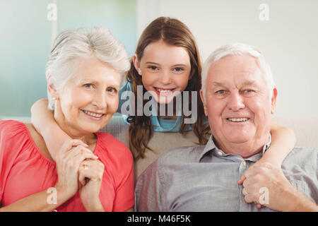 Lächelnde Enkelin umarmen ihre Großeltern im Wohnzimmer Stockfoto