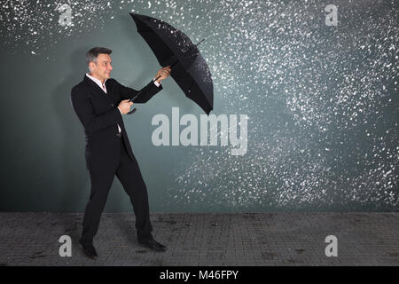 Gereift lächelnd Geschäftsmann mit einem Regenschirm im Schnee auf grauem Hintergrund Stockfoto