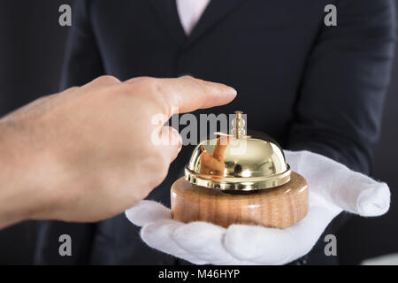 Nahaufnahme von einer Person Hand Ringing Service Bell halten durch Kellner Stockfoto
