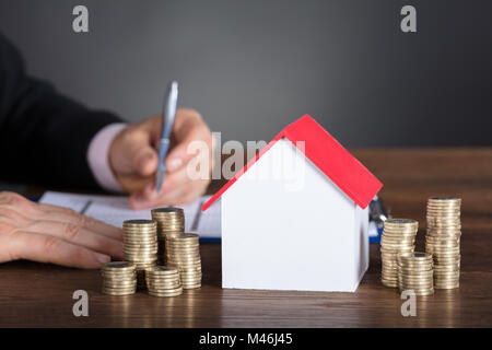 Geschäftsmann Berechnung der Steuer von Modell zu Modell Haus und Stapel von Münzen auf Tisch Stockfoto