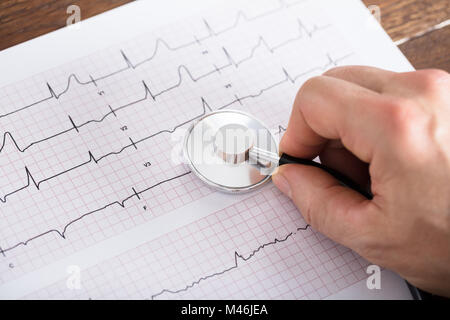 Hohe Betrachtungswinkel der Person Hand mit Stethoskop auf Elektrokardiogramm Diagramm auf hölzernen Schreibtisch Stockfoto