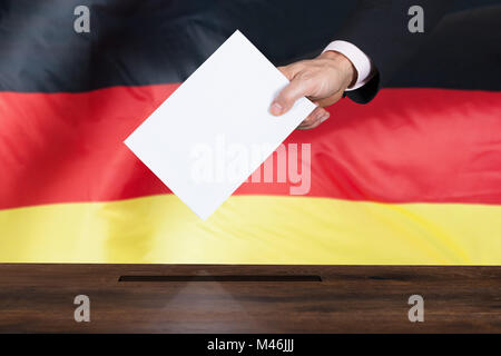 Nahaufnahme einer Person die Abstimmung in einer Wahlurne Vor der deutschen Fahne Stockfoto