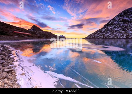 Atemberaubenden Sonnenaufgang auf dem gefrorenen Lago Bianco (Weißer See) mit Transit von Red Train., Bernina, Engadin, Graubünden, Schweiz. Stockfoto