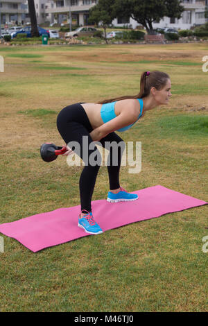 Eine schlanke Frau in Sportkleidung mit einem KETTLEBELL einen tiefen Ausfallschritt im Außenbereich zu tun Stockfoto