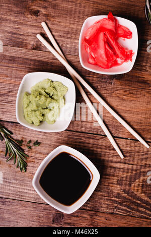 Sticks, Wasabi, Sojasauce und eingelegtem Ingwer für Sushi auf braune Holztisch Hintergrund. Ansicht von oben. Stockfoto