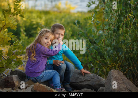 Zeit mit der Familie. Bruder und Schwester sitzen auf Felsen und umarmen. Spaziergang in den Wald. Stockfoto