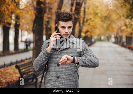 Bild der eleganten Mann gleichzeitig mit Uhr zur Hand und sprechen auf Handy bei seinem Spaziergang im Park Stockfoto