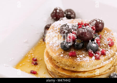 Frühstück Pfannkuchen mit Heidelbeeren, Granatapfel Samen, Kirschen und Puderzucker (staubzucker) und Ahornsirup auf weißem Hintergrund. Stockfoto