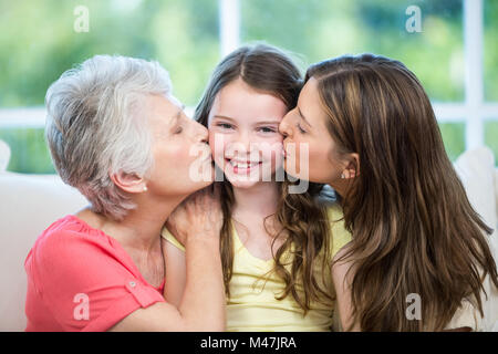 Mutter und Großmutter küssen glückliches Mädchen auf sofa Stockfoto