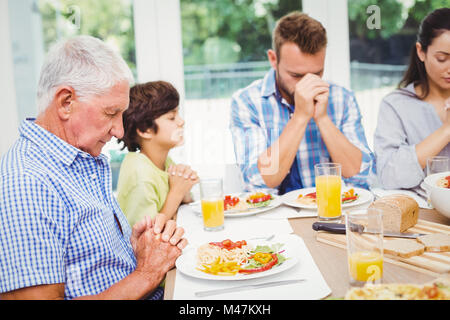 Multi-Generationen-Familie beten beim Sitzen am Esstisch Stockfoto