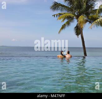 Junges Paar entspannen in Infinity Pool unter Coco Palms Stockfoto