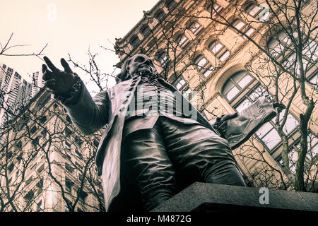 Nach oben Blick auf eine Statue von Benjamin Franklin mit Zweigen und Gebäude für den Hintergrund. Stockfoto