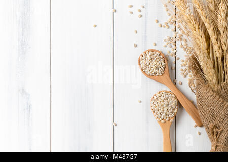 Haufen von zweikorn auf Holz Löffel mit Ohr von Gerste auf weißem Holz Hintergrund, vegetarische Kost, die Ansicht von oben und Platz kopieren Stockfoto