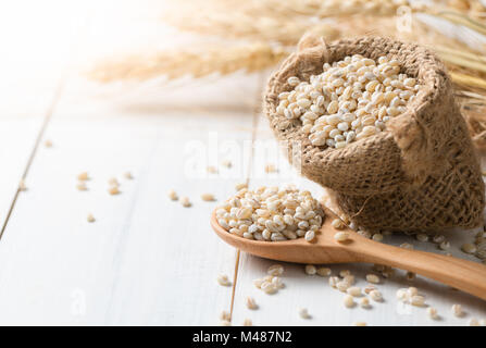 Haufen von zweikorn auf Sack mit Ohren von Gerste auf weißem Holz, vegetarische Kost Stockfoto