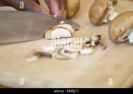 Schwarzer Mann zerkleinern Pilze auf einem hölzernen Schneidebrett Stockfoto