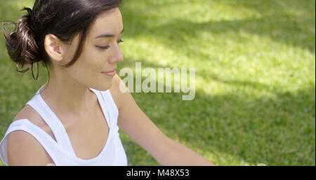 Ruhige junge Frau auf einem grünen Rasen zu meditieren Stockfoto