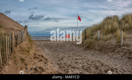 Ein Blick auf die einsamen Strand mit einem Pfad durch die Dünen mit dem rettungsring und die rote Flagge Warnung nicht zu schwimmen. Stockfoto