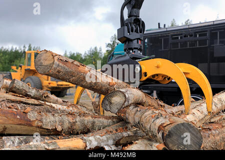 Anmelden Laderausrüstung entlädt Holzbalken an einem Arbeitsplatz mit schweren Maschinen auf dem Hintergrund auseinander. Stockfoto