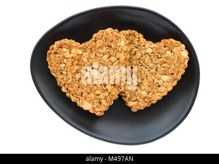 Zwei selbstgebackene herzförmige Erdnuss und Hafer flapjack Kekse für Valentines Tag auf ovalen schwarzen und weißen Hintergrund. Stockfoto