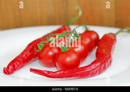 Cherry Tomaten und Hülsen der chili peppers auf Platte Stockfoto