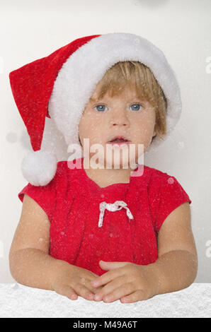 Baby gekleidet wie Santa unter dem fallenden Schnee Stockfoto