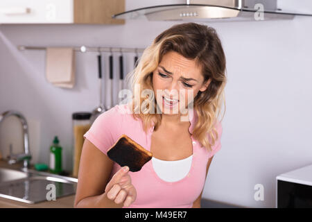 Nahaufnahme der Frustrierte junge Frau mit Toast in der Küche verbrannt Stockfoto