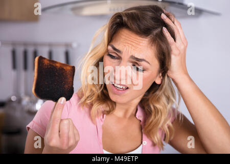 Nahaufnahme der Frustrierte junge Frau mit Toast in der Küche verbrannt Stockfoto