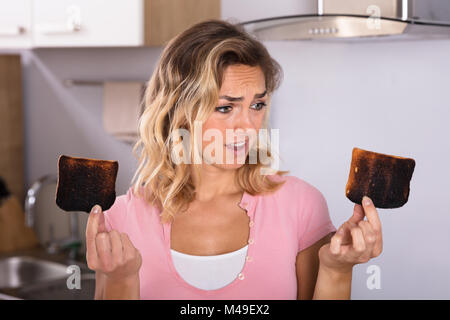 Nahaufnahme der Frustrierte junge Frau mit Toast in der Küche verbrannt Stockfoto