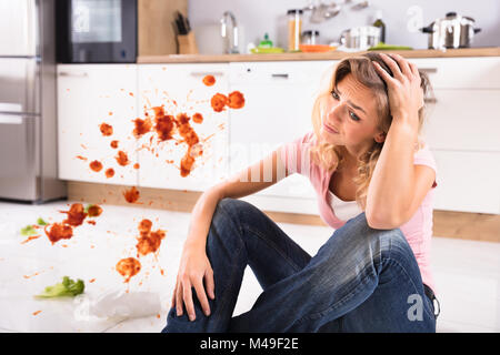 Portrait einer jungen Frau besorgt, in schmutzigen Küche zu Hause sitzen Stockfoto