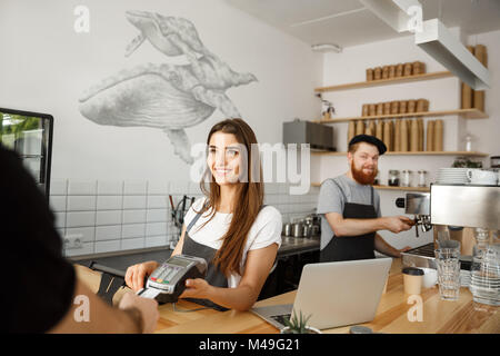 Kaffee Geschäftskonzept - Schöne weibliche Barista, Payment Service für Kunden mit Kreditkarte und lächelnd, während an der Theke in der modernen Coffee Shop. Stockfoto