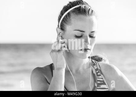 Erfrischende wilden Meer Seite Training. fit gesunde Frau in Sportkleidung auf der Seeküste mit Kopfhörern hören von Musik Stockfoto