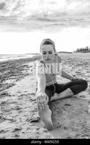 Erfrischende wilden Meer Seite Training. Aktive passende Frau in Sports Gear auf der Seeküste Stretching Stockfoto