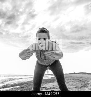 Erfrischende wilden Meer Seite Training. Junge aktive Frau in Sportkleidung, der am Ufer des Meeres ausdehnen Stockfoto