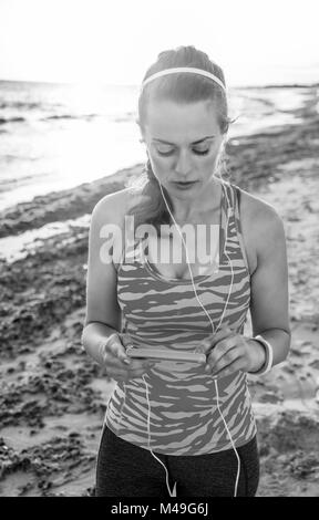 Erfrischende wilden Meer Seite Training. Aktiv fitness Frau in Sportkleidung auf der Seeküste mit Kopfhörern hören von Musik Stockfoto