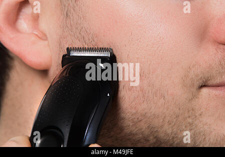 Trimmer auf Unrasierten Gesicht Nahaufnahme. Mann Rasieren mit dem elektrischen Rasierer. Stockfoto