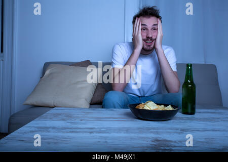 Junger Mann vor dem Fernseher nachts mit Chips und Bier Stockfoto